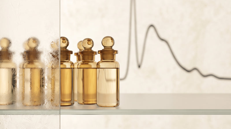 Amber laboratory glass vials under soft golden studio light with a faint blurred chromatography curve in the background, warm champagne and ivory tones