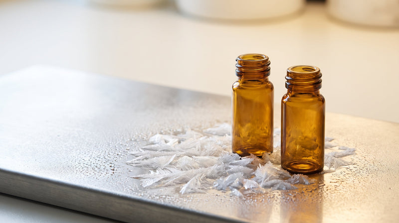 Amber research vials on a frosted chilled surface with fine ice crystals, cold-chain handling