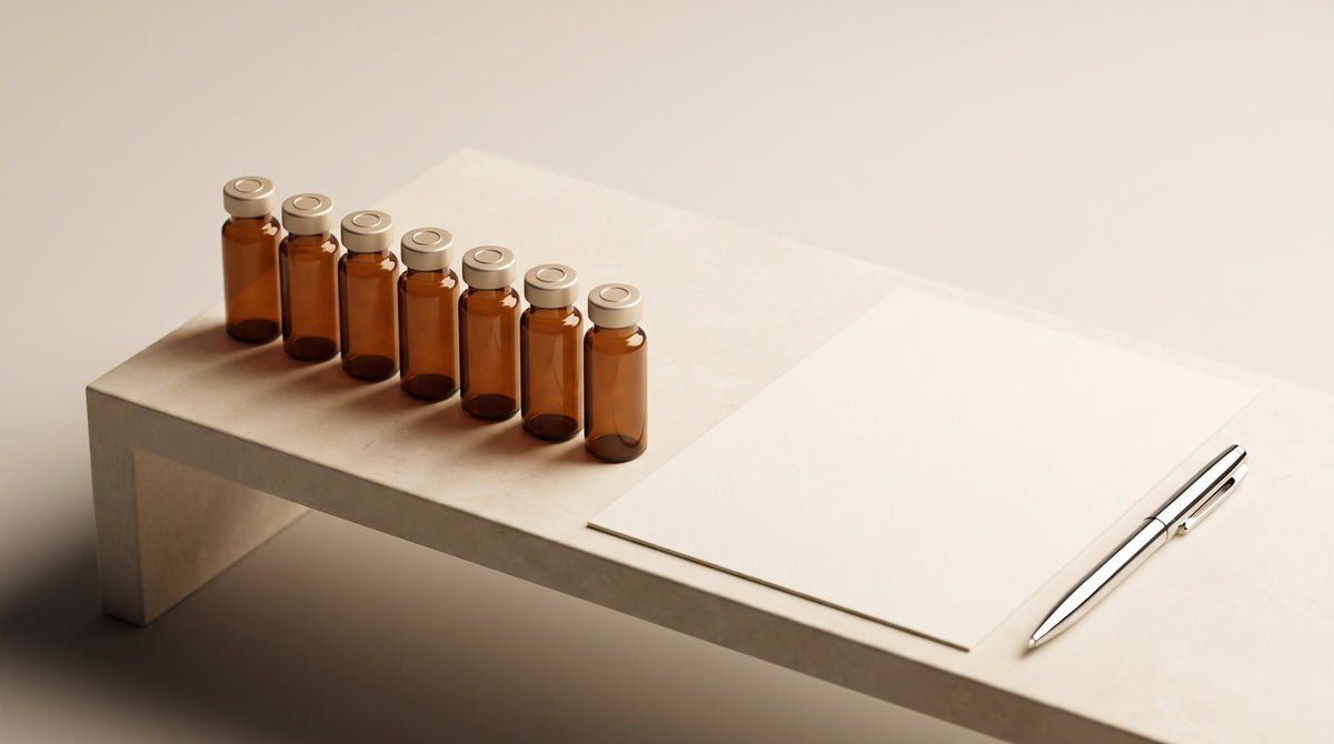 Amber laboratory vials arranged beside a blank documentation sheet on a stone bench, warm gold and ivory tones