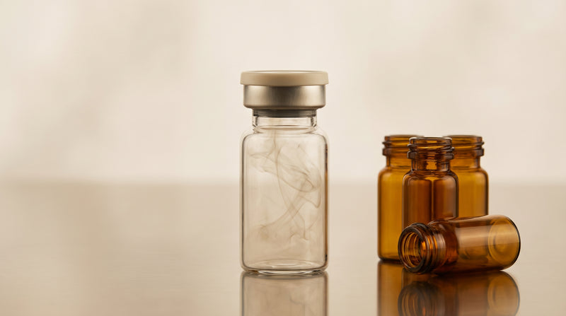Amber laboratory glass vials with rubber septa and crimp caps on a reflective surface, warm gold and champagne tones, soft studio lighting