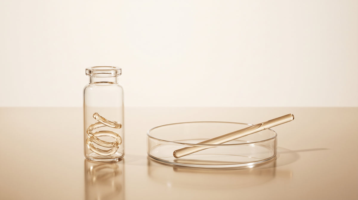Abstract laboratory still life with a coiled glass ring beside a straight glass rod in warm gold and ivory tones