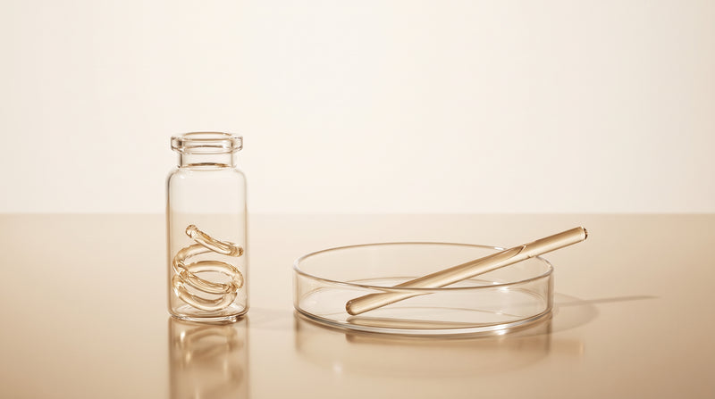 Abstract laboratory still life with a coiled glass ring beside a straight glass rod in warm gold and ivory tones