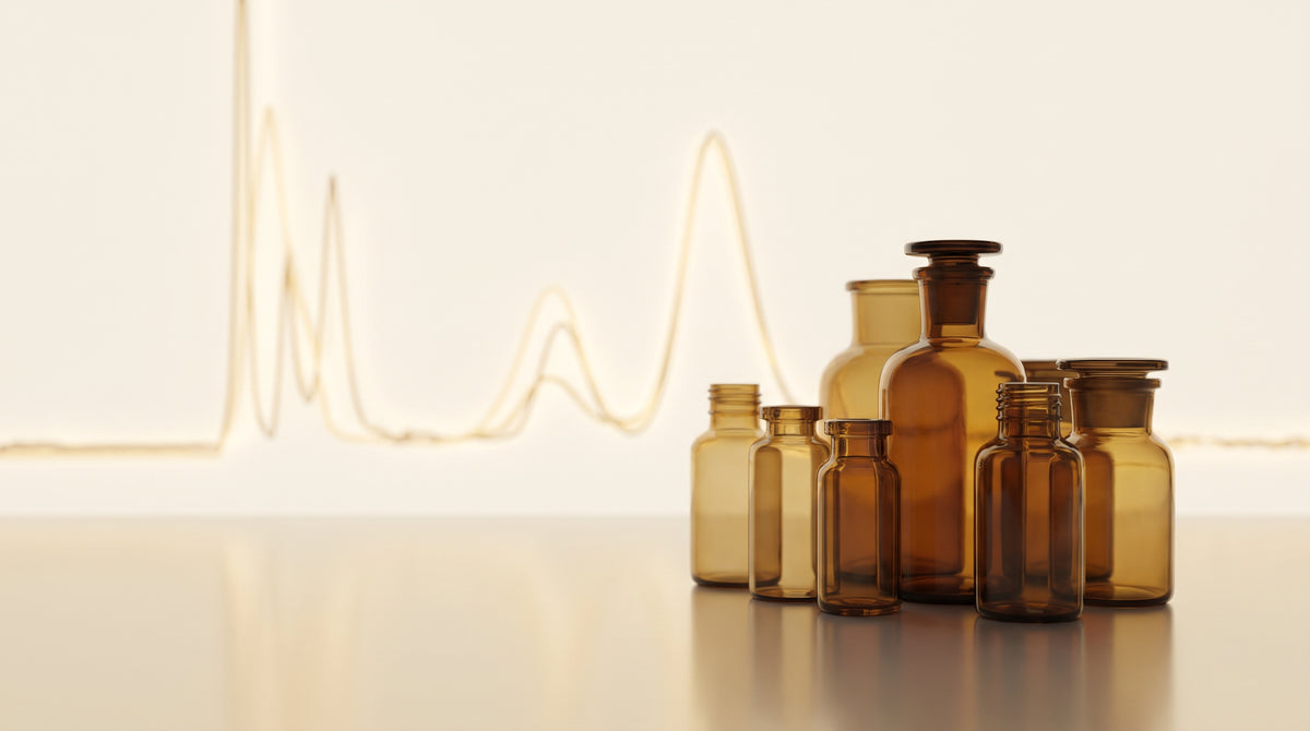 Amber laboratory glass vials on a reflective surface with a faint glowing chromatography curve in warm gold and champagne tones